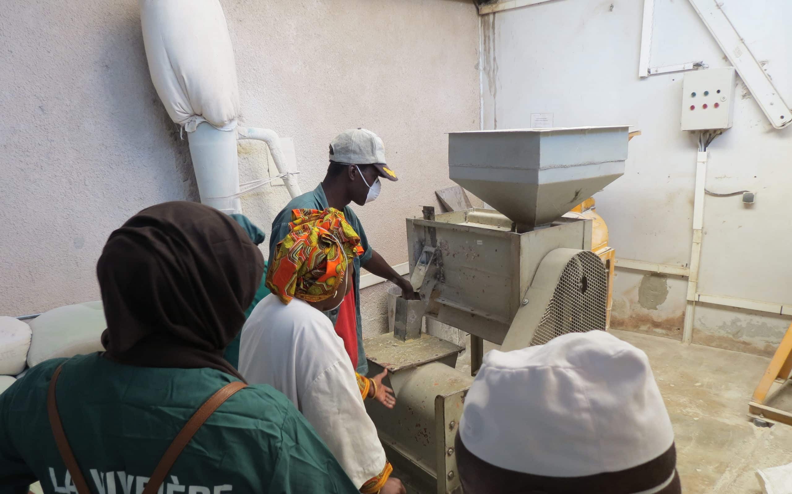 Bineta y los empleados de La Vivriére hacen una demostración de cómo utilizar la maquinaria utilizada para procesar la harina de mijo.