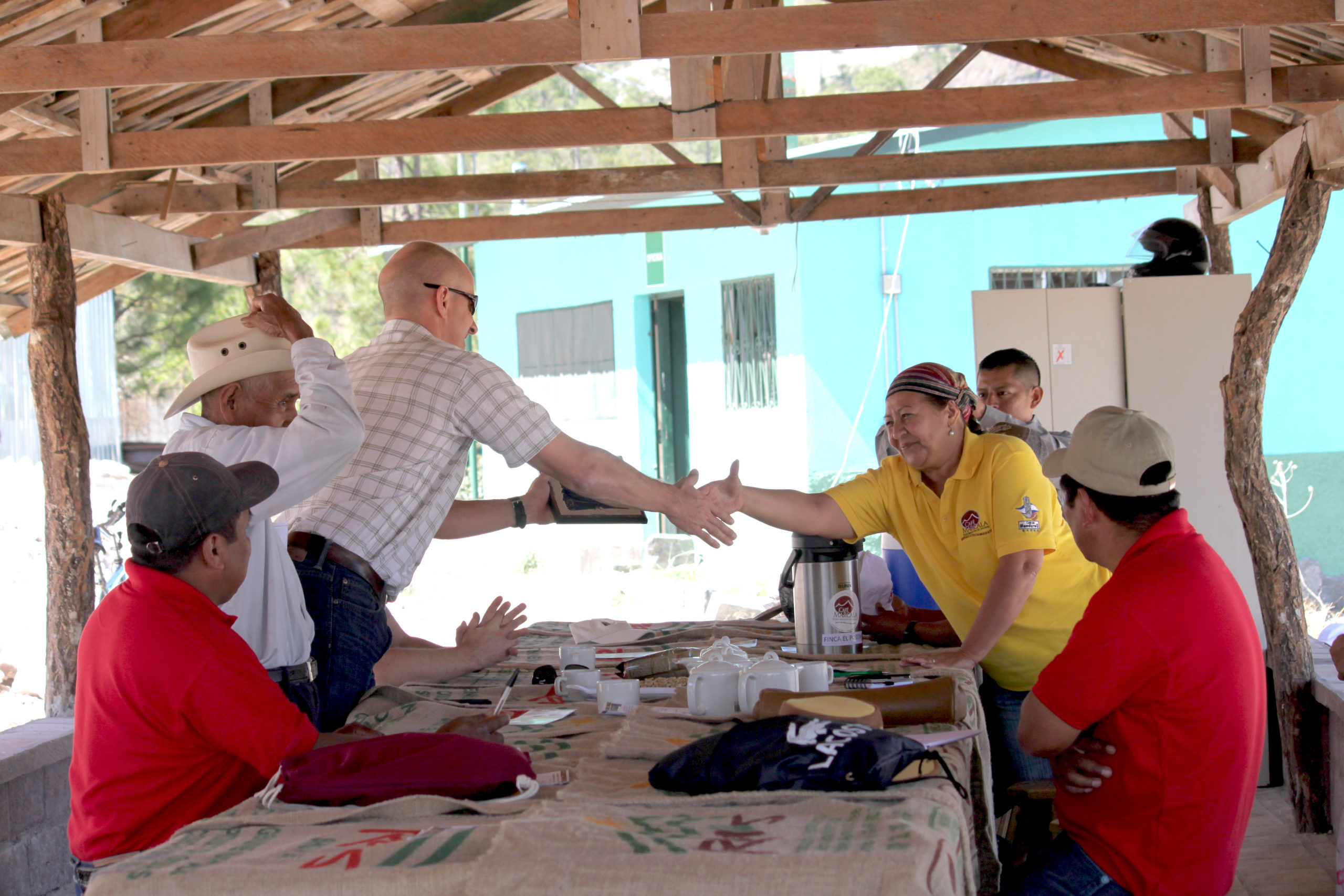 Melba Sosa of RAOS shakes hands with Willy Foote across a table with other members f the cooperative.
