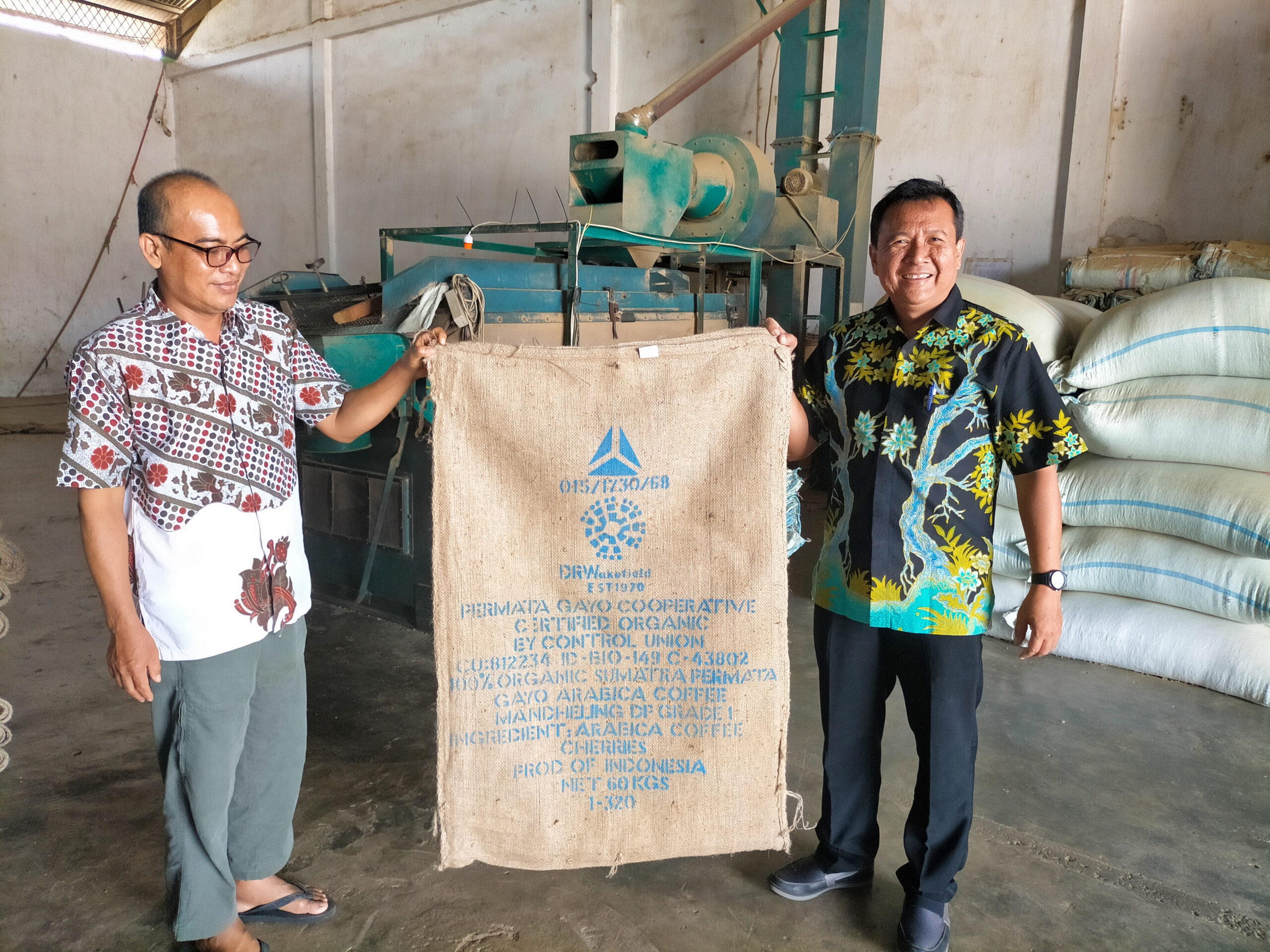 Pak Syamsudin, left, from the Export Division of Permata Gayo, and USAID/Indonesia Project Management Specialist Mispan Indarjo, right, display a burlap sack with the cooperative’s name and certifications listed at their warehouse in Medan on Sumatra. Credit: Root Capital.