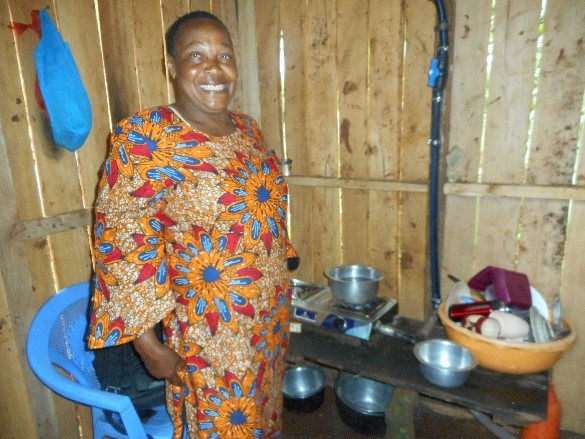 A Kenyan smallholder macadamia nut farmer proudly shows off her “new” clean cooking gas system thanks to her two dairy cows and biodigester system in Kenya. Credit: Root Capital.